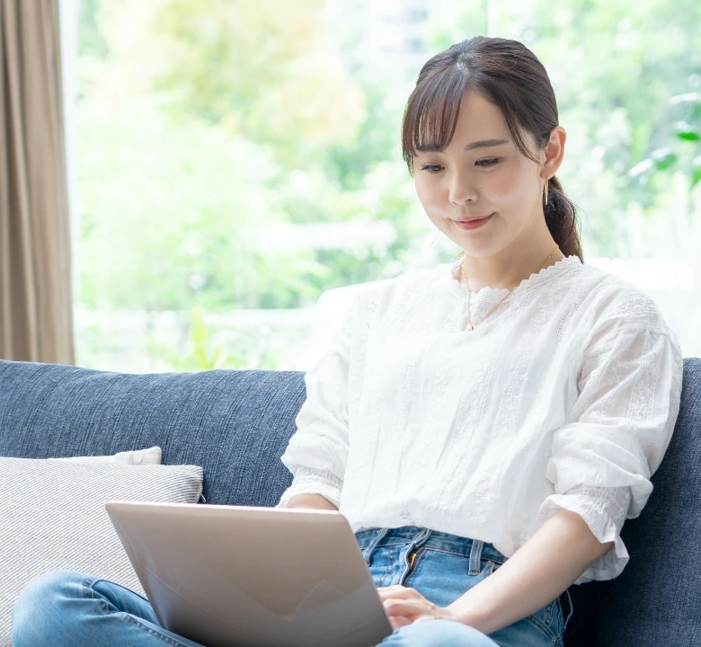 女性が在宅でパソコンを見ながらソファに座っている様子